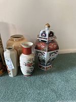 Photo of multiple Asian themed urns and umbrella holders showing their decoration and shapes on carpet.