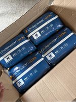 Top view of open box containing four unopened packs of McKesson Underwear Ultra adult diapers size medium.
