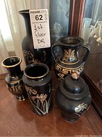 Photo showing five matching black and gold decorative urns and vases arranged on a surface.