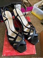 Black strappy heeled sandals with a cross strap design shown on original red East 5th box.