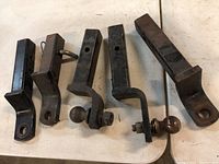 Five trailer hitches laid out side by side on a flat surface showing general condition and variety.