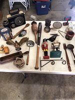 Overview of various vintage items on a table including radio, kitchen utensils, figurines, brass eagle, wooden duck decoys, etc.
