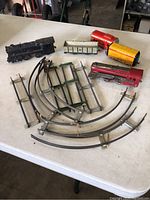Photo showing five antique toy train cars in various colors along with several metal track pieces including straight and curved sections.