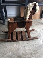 Side view of child's wooden rocking horse showing yarn mane, leather saddle, and wooden rocker base.