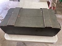 Closed dark painted wooden foot locker with visible wear on the lid and edges