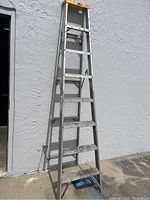 Full view of the 8-foot tall aluminum step ladder leaning against a textured wall, showing structure and condition.