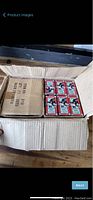 Open cardboard factory case showing multiple boxed sets of Monopoly tile magnets arranged inside alongside sealed box