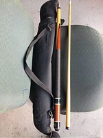 Full view of two-piece pool cue stick next to black zippered bag with shoulder strap.