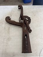 Full view of the antique railroad spike puller showing body, handle, and hook jaws on a white surface.