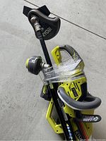 Cluster of three Ryobi 40V outdoor power tools wrapped together on floor: string trimmer, hedge trimmer, and blower all visible with yellow and black coloring.