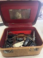 Open vintage sewing box showing tangled electrical cords and sewing machine pedals inside, mirror visible on lid.