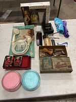 Photo showing full lot on table including boxed perfume set, portable shower, grooming brushes, vintage razors, compact, small towels, and other beauty items.
