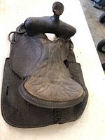 Top view of vintage horse saddle showing embossed floral design on side panels and quilted padded seat.