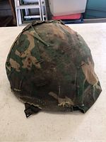 Front view of the vintage military army helmet showing the camouflage fabric cover with wear and fraying edges.
