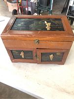 Front view of wooden jewelry box showing painted oriental figures on top and front panels, with visible latch hardware and drawer.