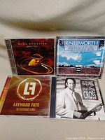 Four music CDs arranged in a square: Mark Knopfler Golden Heart, Knebworth live concert, Leeward Fate No Ordinary Kind, and Phil Manzanera Guitars and Cross.