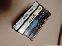 Four metal music cassette tapes stacked showing spines and titles including Judas Priest, Queensryche, Faith No More, Dream Theater