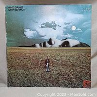 Front cover of John Lennon Mind Games album with surreal face and field artwork under partly cloudy sky with celestial objects.