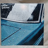 Front cover of Peter Gabriel vinyl album showing part of a blue car door and window with rain droplets and the artist name on top left.