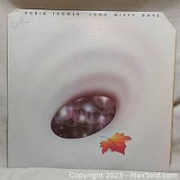 Front cover of Robin Trower's Long Misty Days album with an abstract egg-like shape and a red maple leaf, showing some wear and bent corners.