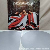 Front album cover of The Who's The Kids Are Alright with band wrapped in Union Jack flag. Two vinyl records displayed in white sleeves.