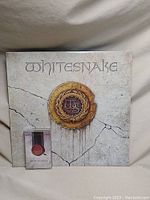 Whitesnake vinyl record album cover with white background and circular gold design, showing some age marks and cracks.