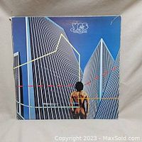 Front cover of Yes 'Going for the One' vinyl album showing a person standing looking at tall modern buildings. The album cover has some wear with corner creases.