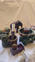 Photo showing two ceramic green elephant planters, a carved wooden elephant, and part of a carved sandstone elephant.