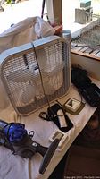 Photo of white box fan with metal grill, two Honeywell thermostats, Wahl hair trimmers, and Aiptek camera on white cloth.