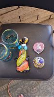 Lot of Murano glass items displayed on a black surface including a clown figurine wearing blue glasses, two multicolored glasses, a bell-shaped paperweight, and a pink heart-shaped flower paperweight.
