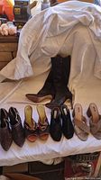 Lot of five pairs of women's shoes arranged side by side on a white surface, includes tall black boots, ankle boots, open-toe heels, and wedge sandals.