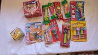 Overview of eight assorted PEZ dispensers and one Simpsons watch box on white surface