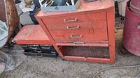 Two red metal tool boxes, one larger and one smaller, placed outside on the ground. Both have wheels and signs of wear and rust.