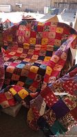 Quilt one draped over a fabric sofa, showing a patchwork of colorful squares in red, pink, yellow, purple, and brown hues with various patterns.