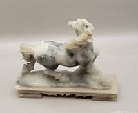 Front right angled view of the horse jade sculpture showing white and gray mottled jade with carved mane and tail, mounted on a rectangular base.