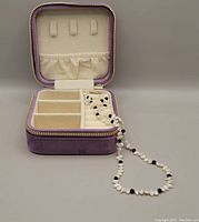The pearl and onyx necklace displayed neatly inside an open purple velvet travel box with multiple compartments and hooks for jewellery storage.
