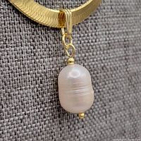 Close-up of large freshwater pearl pendant with gold bail attached to a polished, flat chain.