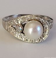 Close-up front view of white gold ring with pearl and small diamond set in engraved bezel.
