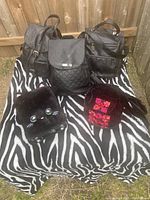 Five black backpacks displayed on a zebra print cloth outdoors. Mix of faux leather, velvet, and quilted materials, various closure types.