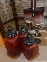 Three tall amber gradient glass hurricane candleholders with shell decorations inside, one visibly chipped