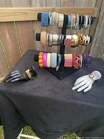 Assorted costume bracelets displayed on a black stand with two hand mannequins showing individual bracelets. Variety of colors and materials visible including plastic, metal, beads, and rhinestones.