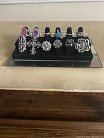 Twelve assorted colorful crystal stretch costume rings displayed on black ring display stand.