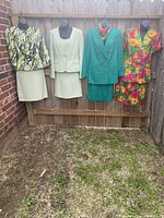 Four ladies skirt suit sets displayed on mannequins: green/black Isabella 2-piece, sage 3-piece Tahari set, double button green 2-piece with scarf, printed multicolor linen and silk 2-piece.