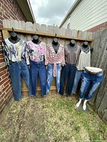 Full display of 6 pairs of ladies jeans on mannequins with 5 blouses hung above fence and one mannequin wearing jeans with a leopard print belt.