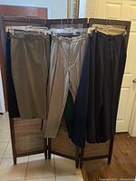 Photo showing three pants (olive green, checked beige, black) hanging on a wooden room divider