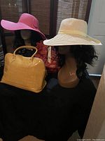 Two floppy hats on mannequins and a yellow Arcadia patent handbag on black cloth