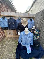 Four denim jackets, a black beaded jacket, jean vest, black cowboy hat, and scarf displayed on mannequins and hangers outdoors