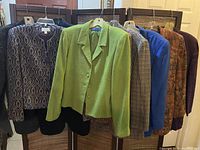 Nine ladies blazers in various colors and patterns hung on hangers, showing textures and colors including green, blue, purple, and prints.