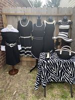 Full view of five dresses displayed on mannequins outdoors, plus a black and white zebra fabric covered table with shoes, purse and hat