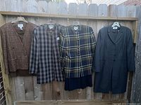 Four ladies suits hanging on fence including multi-color rust blazer and skirt, two plaid John Meyer blazers and skirts, and Kasper long navy jacket with matching tunic dress